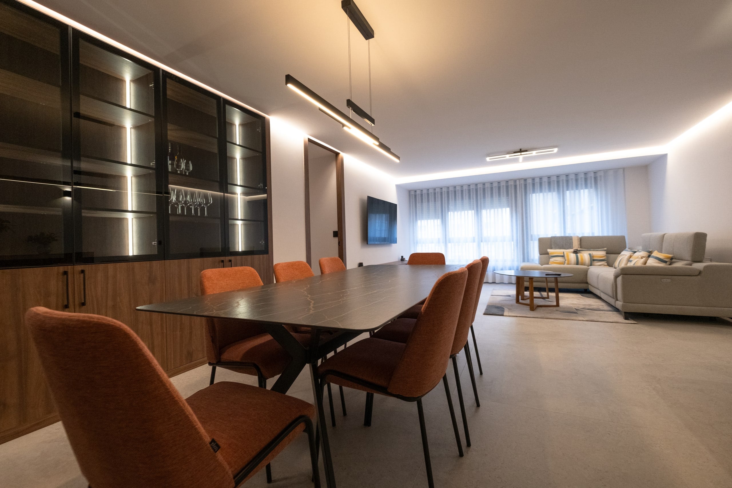 Salón comedor continuo con vitrinas de nogal y vidrio, mesa de comedor y zona de estar al fondo