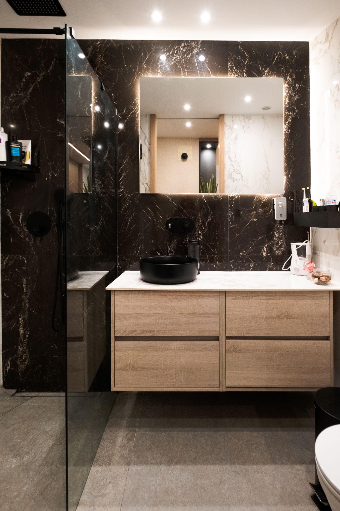 Baño con revestimiento de mármol oscuro y mueble de madera
