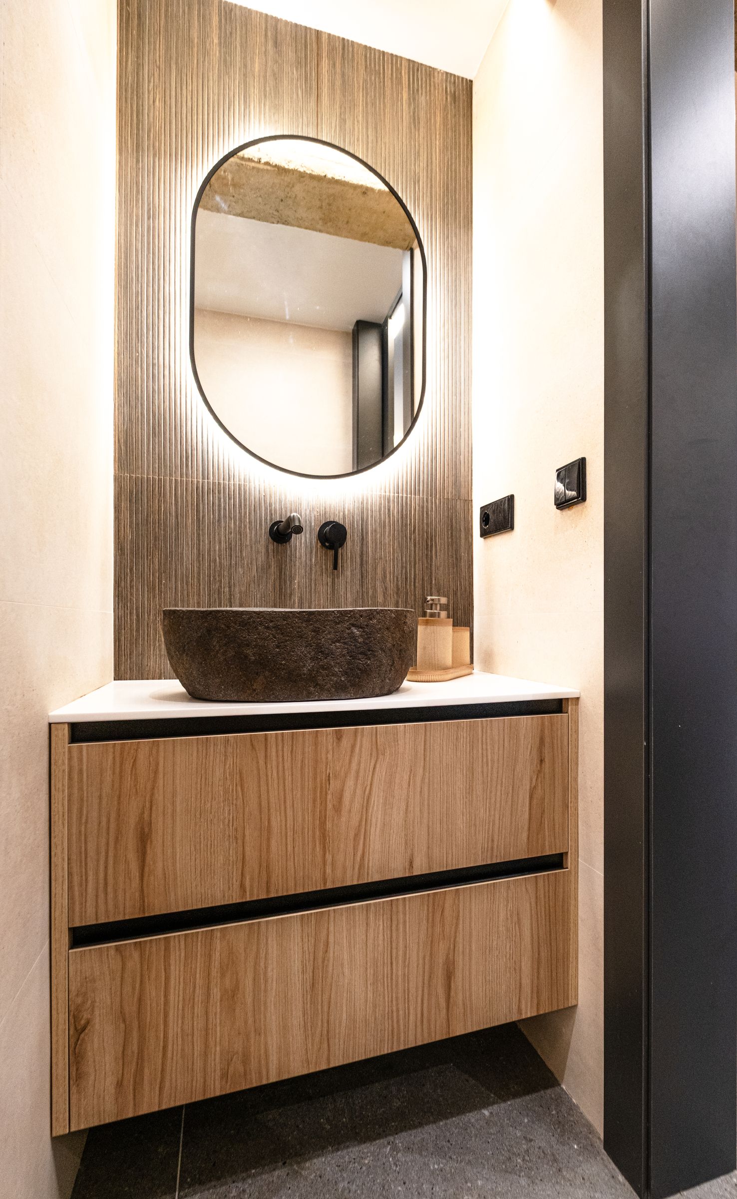 Baño con lavabo de piedra y espejo ovalado de luz cálida
