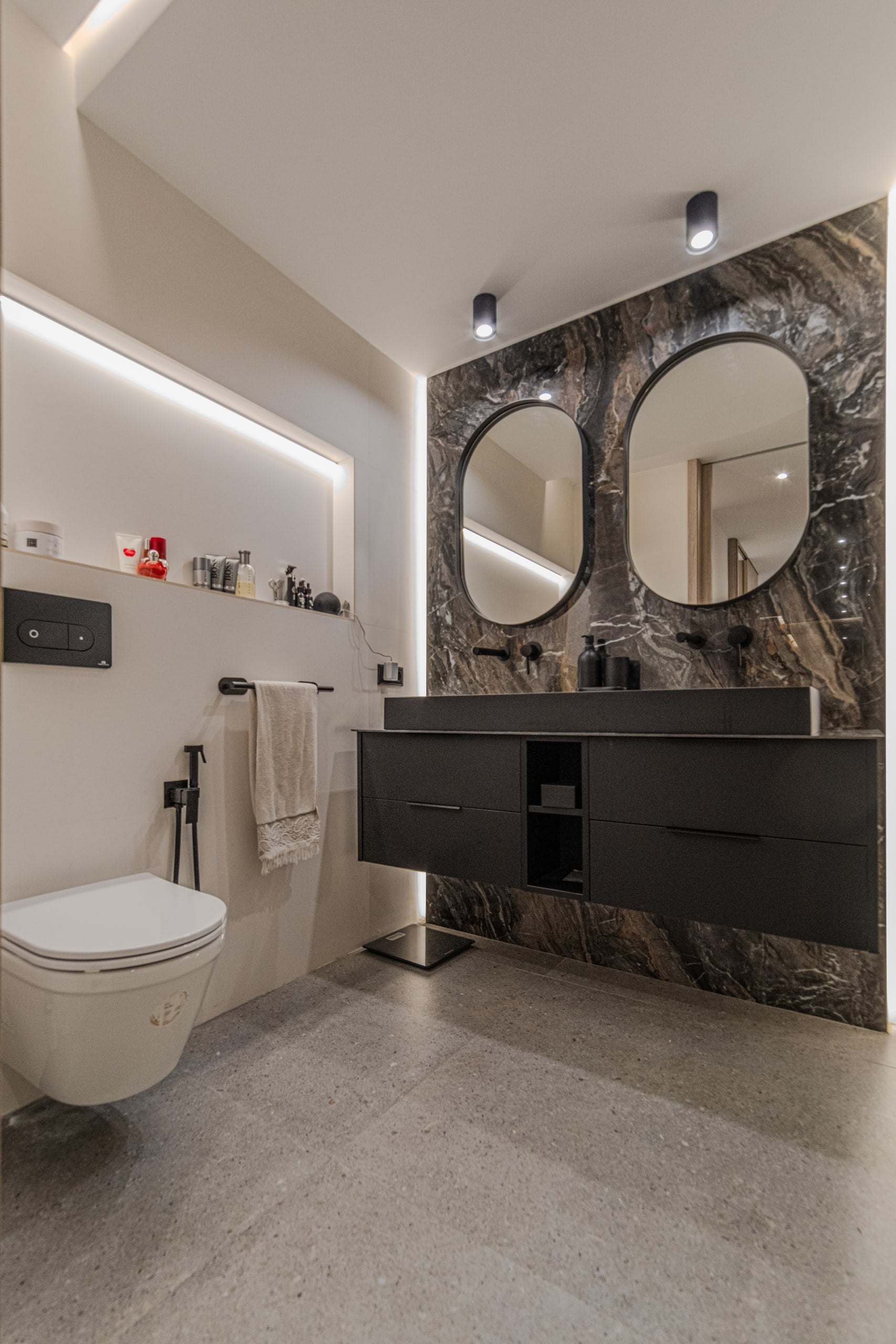 Baño con revestimiento de piedra oscura, doble espejo redondo y mueble suspendido