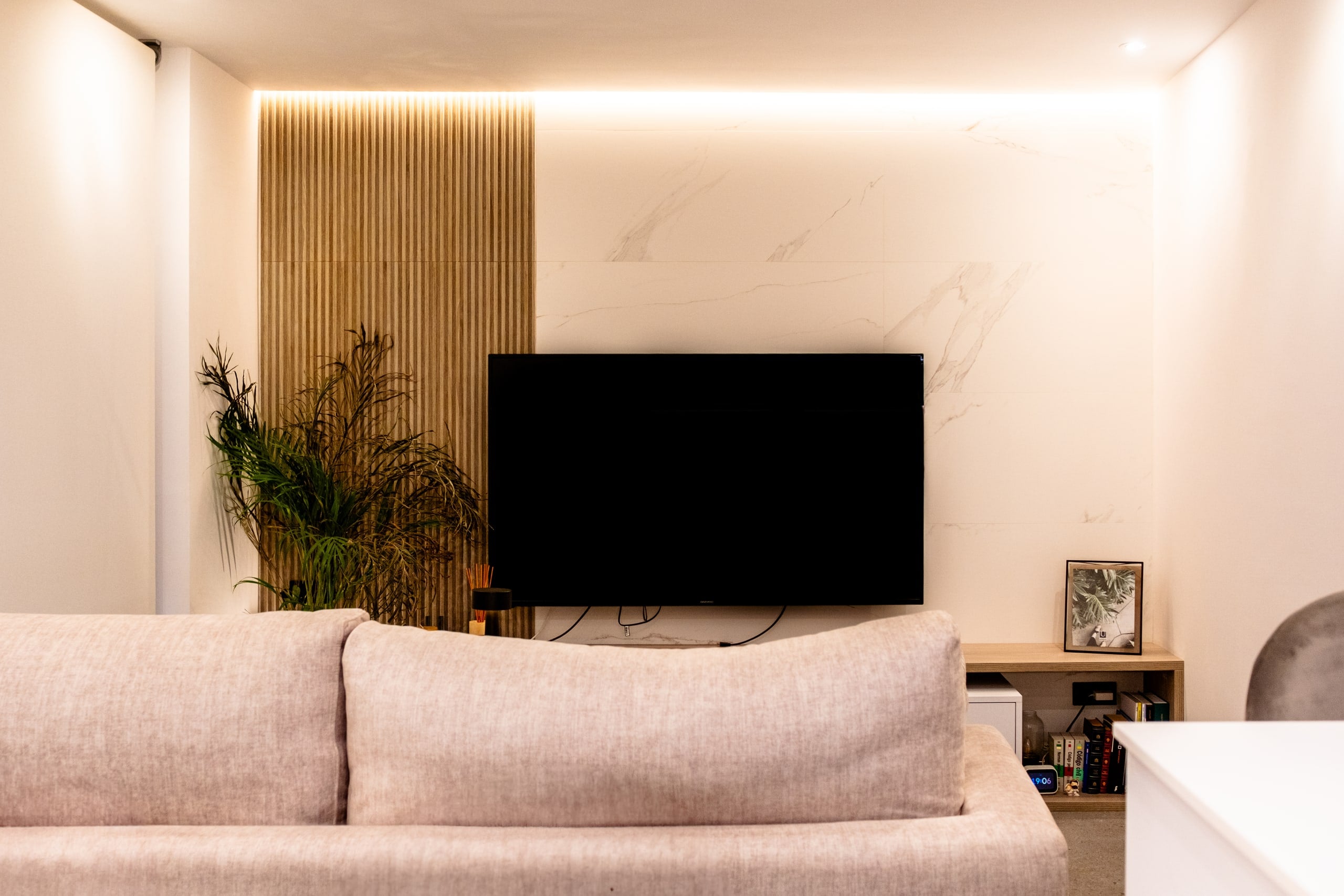 Salón con panel de listones de madera, mueble de televisión y luz indirecta